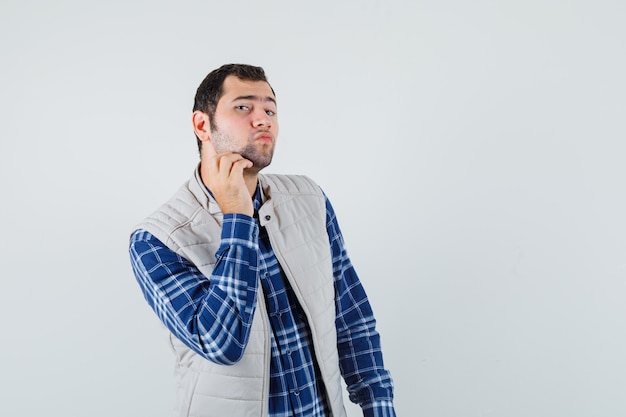 Giovane maschio che tocca la sua barba in camicia, vista frontale giacca senza maniche.