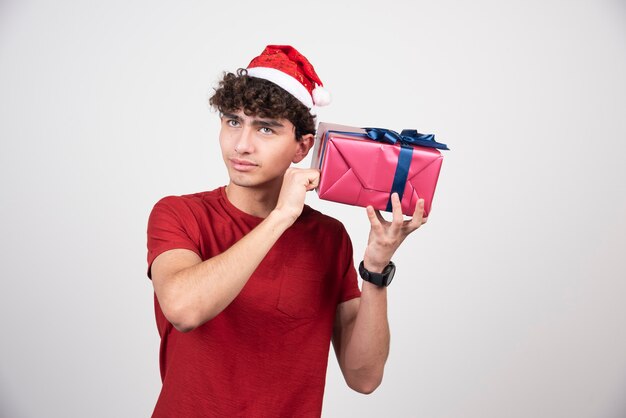 Giovane maschio con cappello da Babbo Natale che cerca di capire cosa c'è dentro la scatola.