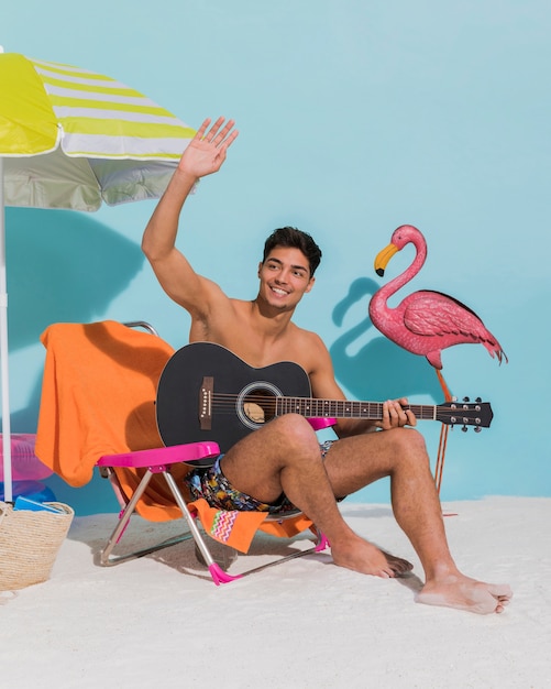 Giovane maschio con chitarra agitando la mano sulla spiaggia