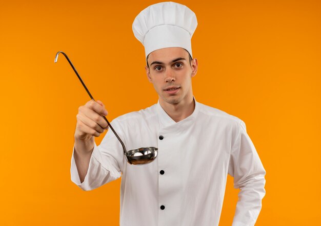 giovane maschio cool chef indossa uniforme holding mestolo sulla parete gialla isolata