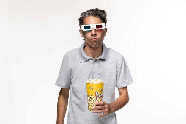 Giovane maschio di vista frontale che mangia popcorn in occhiali da sole d su superficie bianca