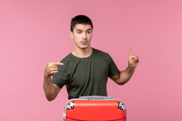 Giovane maschio di vista frontale che prepara per la vacanza con la grande borsa sullo spazio rosa pink