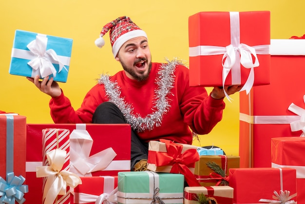 Giovane maschio di vista frontale che si siede intorno ai regali di Natale su colore giallo