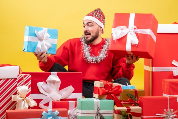 Giovane maschio di vista frontale che si siede intorno ai regali di Natale su fondo giallo