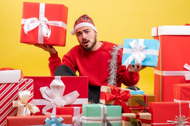 Giovane maschio di vista frontale che si siede intorno ai regali di Natale su fondo giallo