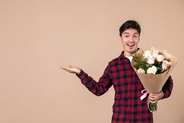 Giovane maschio di vista frontale che tiene bei fiori sulla parete marrone