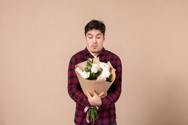 Giovane maschio di vista frontale che tiene bei fiori sulla parete marrone