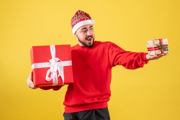 Giovane maschio di vista frontale che tiene i regali di natale su fondo giallo