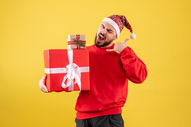 Giovane maschio di vista frontale che tiene i regali di natale su fondo giallo