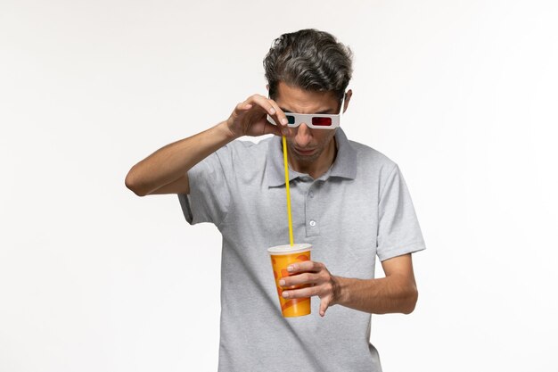 Giovane maschio di vista frontale che tiene soda in occhiali da sole d sul godimento di film a distanza della parete bianca solitario