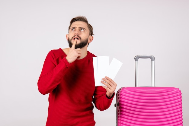 Giovane maschio di vista frontale con il sacchetto rosa e che tengono i biglietti sul turista di estate di viaggio di volo di vacanza di viaggio di colore della parete bianca