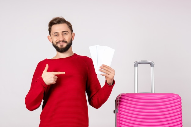 Giovane maschio di vista frontale con la borsa rosa e che tiene i biglietti sul turista di viaggio di volo di vacanza di colore della parete bianca