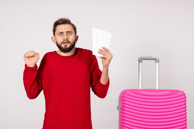 Giovane maschio di vista frontale con la borsa rosa e che tiene i biglietti sulla foto di vacanza turistica di viaggio di colore di viaggio della parete bianca