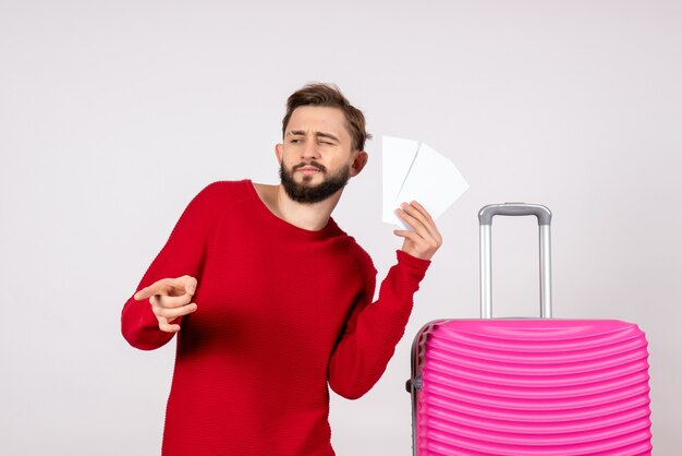 Giovane maschio di vista frontale con la borsa rosa e che tiene i biglietti sulla vacanza turistica di viaggio di volo di viaggio di colore della parete bianca