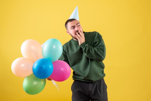 Giovane maschio di vista frontale con palloncini colorati su sfondo giallo