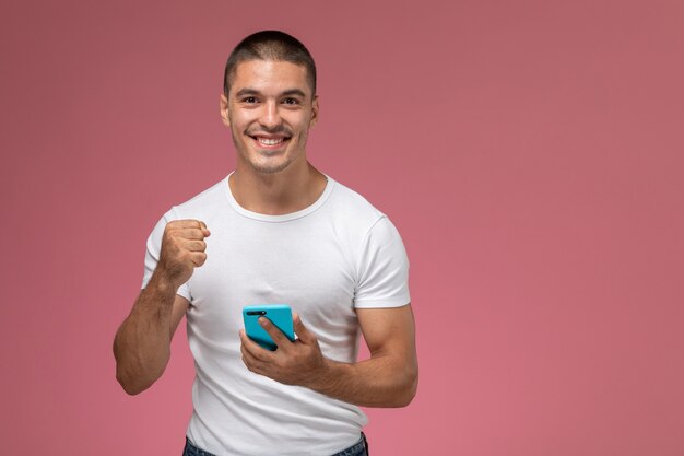Giovane maschio di vista frontale in camicia bianca usando il suo telefono con l'espressione felice su fondo rosa