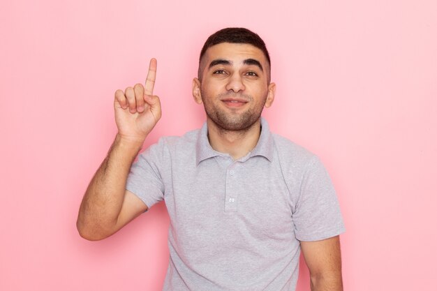 Giovane maschio di vista frontale in camicia grigia che posa con il dito alzato sul colore rosa