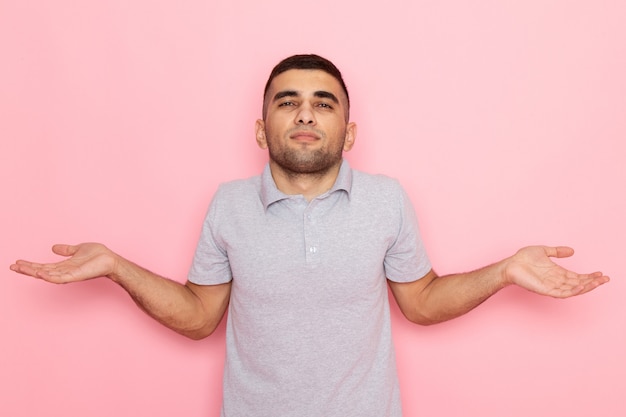 Giovane maschio di vista frontale in camicia grigia che posa con l'espressione sconosciuta sul colore rosa