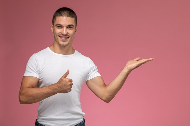 Giovane maschio di vista frontale in maglietta bianca che posa e che sorride sui precedenti rosa