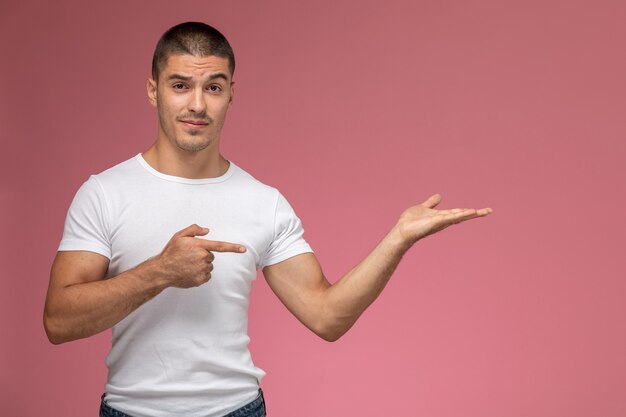 Giovane maschio di vista frontale in maglietta bianca che propone e che indica sulla scrivania rosa