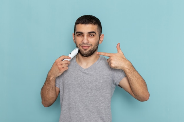 Giovane maschio di vista frontale in maglietta grigia che rade la sua barba sulla schiuma dei capelli maschii della barba da barba blu ghiaccio