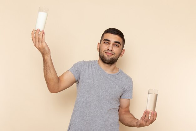 Giovane maschio di vista frontale in maglietta grigia che tiene bicchiere di latte d'acqua su beige