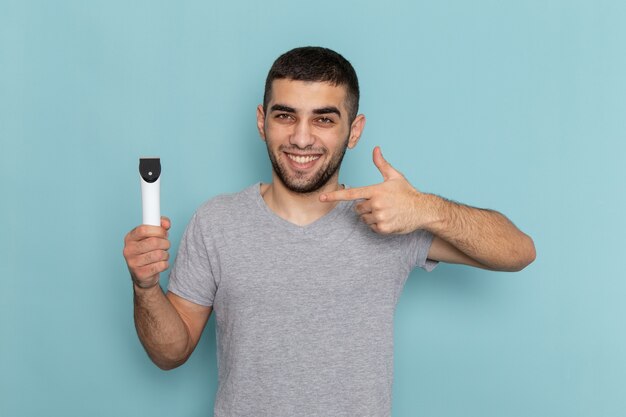 Giovane maschio di vista frontale in maglietta grigia che tiene il rasoio elettrico sulla schiuma dei capelli maschii della barba da barba blu