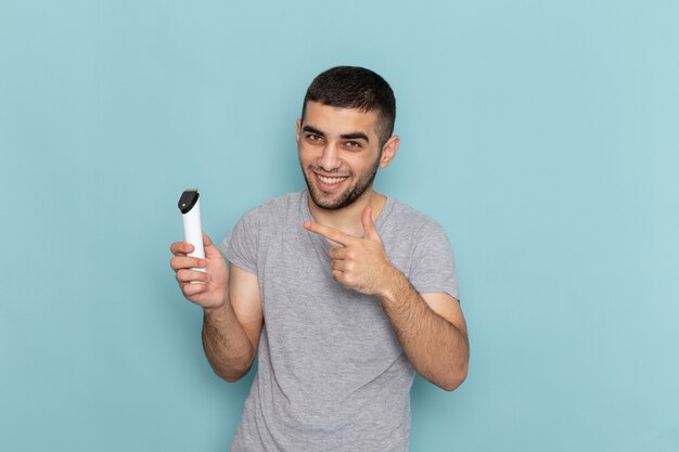 Giovane maschio di vista frontale in maglietta grigia che tiene il rasoio elettrico sulla schiuma dei capelli maschii della barba da barba blu