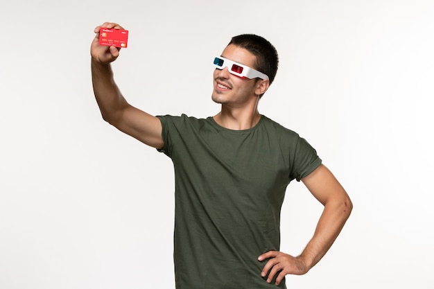 Giovane maschio di vista frontale in maglietta verde che tiene la carta di credito in occhiali da sole d sul film del cinema solitario della pellicola bianca della parete