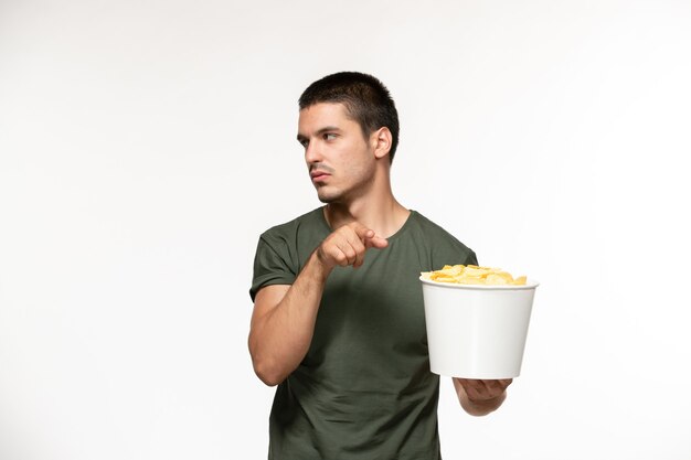 Giovane maschio di vista frontale in maglietta verde che tiene le patatine fritte sulla persona solitaria del cinema di film di film della parete bianca