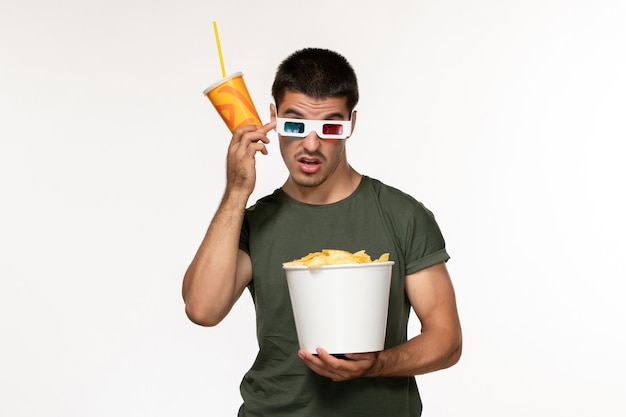 Giovane maschio di vista frontale in maglietta verde che tiene soda di patatine fritte in occhiali da sole d sul cinema di film solitario maschio della pellicola bianca della parete