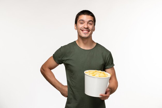 Giovane maschio di vista frontale in maglietta verde con le patatine fritte che sorride sul cinema di film solitario maschio della persona del film della parete bianca