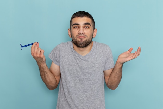 Giovane maschio di vista frontale in t-shirt grigia che tiene il rasoio in posa sul colore della schiuma di capelli maschii della barba da barba blu