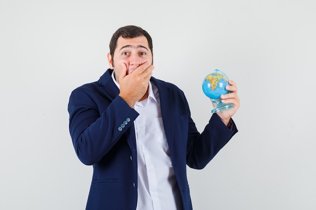 Giovane maschio in camicia e giacca tenendo il globo della scuola e guardando sorpreso