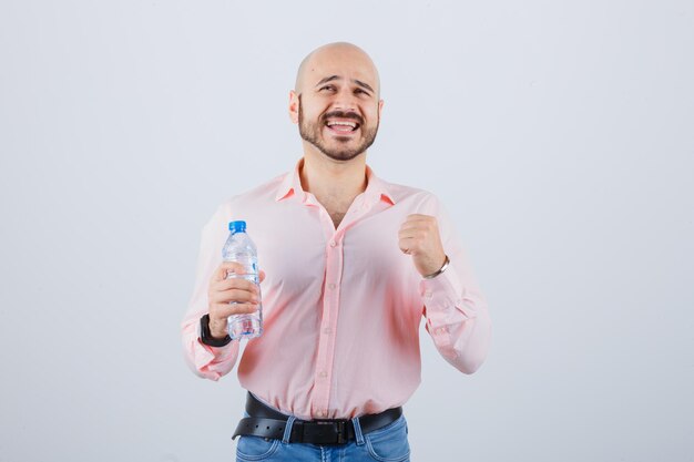 Giovane maschio in camicia, jeans che mostra il gesto del vincitore e sembra fortunato, vista frontale.