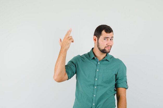 Giovane maschio in camicia verde che mostra il gesto della pistola e sembra carino, vista frontale.