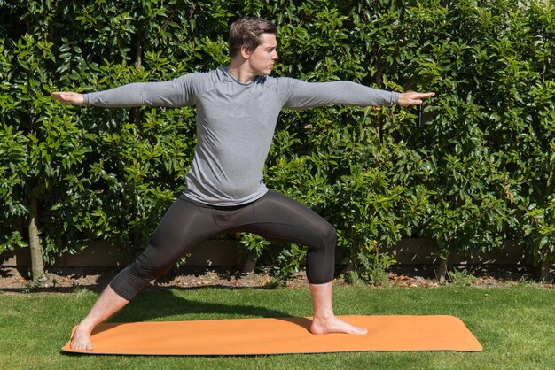 Giovane maschio in forma che pratica yoga e fa la posa del guerriero all'aperto