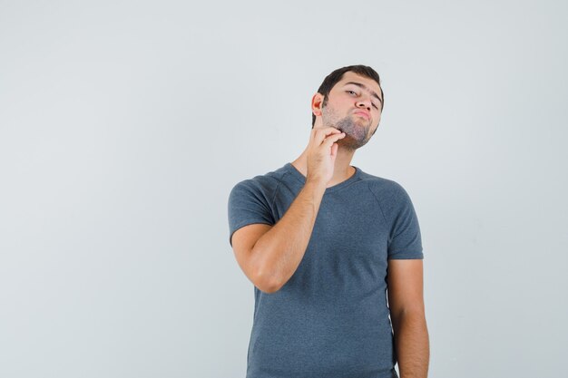 Giovane maschio in maglietta grigia che tocca la sua barba e che sembra elegante