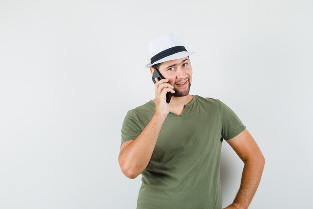 Giovane maschio in maglietta verde e cappello parlando al cellulare e sorridente