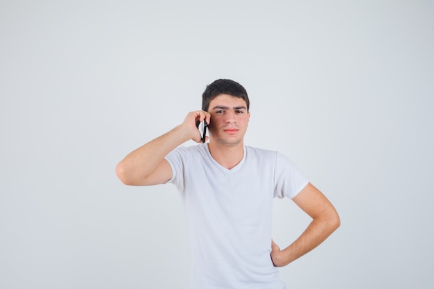 Giovane maschio in t-shirt parlando al telefono cellulare e guardando fiducioso, vista frontale.