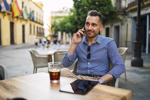 Giovane maschio in un abito formale, seduto in un caffè all'aperto, parlando al telefono