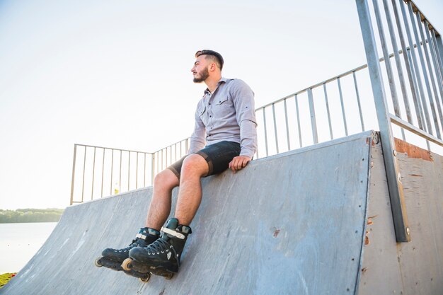 Giovane maschio rollerskater che si siede nel parco del pattino