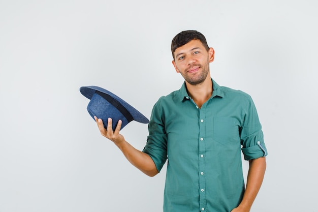 Giovane maschio sorridente e tenendo il cappello in camicia