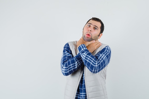 Giovane maschio stringendo il collo con le mani in camicia, giacca senza maniche e guardando soffocato, vista frontale.