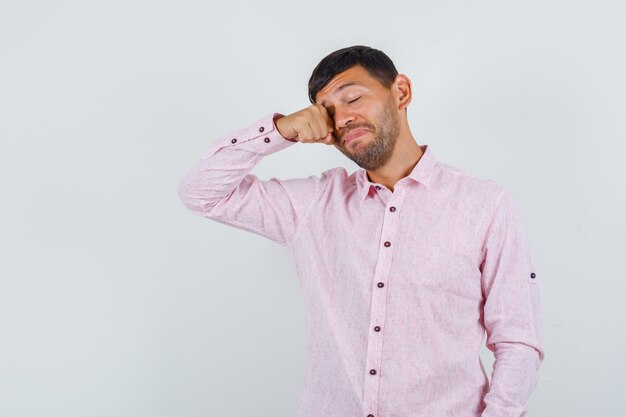 Giovane maschio strofinando gli occhi in camicia rosa e sembra assonnato. vista frontale.