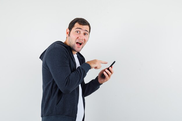 Giovane maschio utilizzando il telefono cellulare in t-shirt, giacca e guardando allegro. .