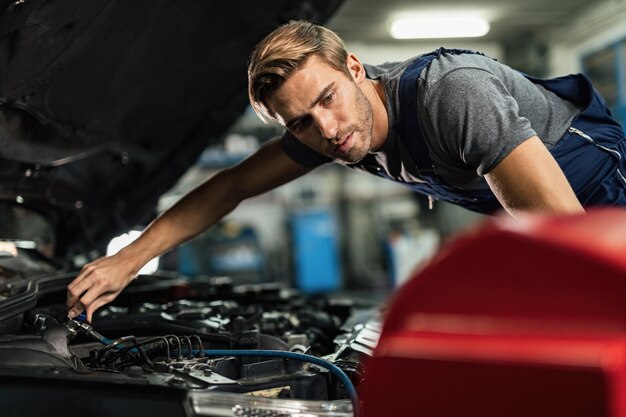 Giovane meccanico che lavora al sistema di aria condizionata di un'auto in officina