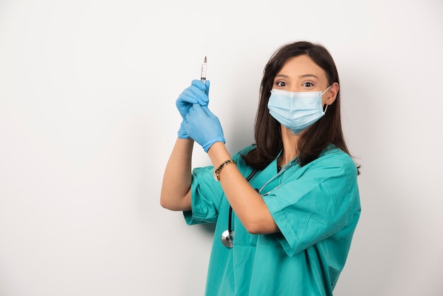 Giovane medico con maschera medica e siringa su sfondo bianco.