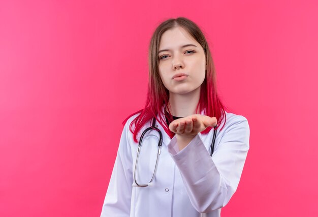 giovane medico donna che indossa uno stetoscopio abito medico che mostra il gesto di bacio sulla parete isolata rosa
