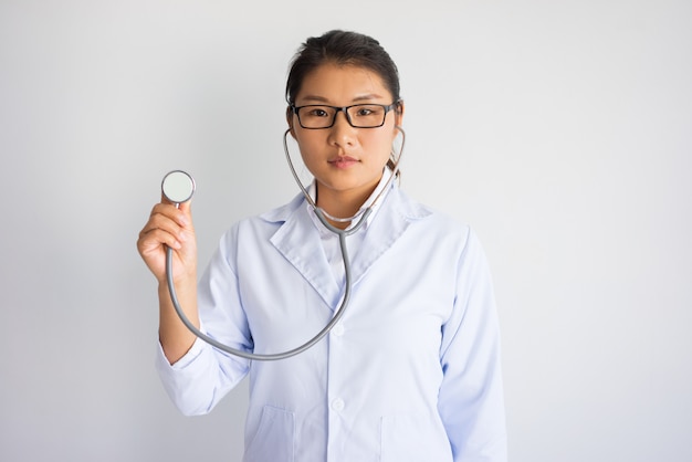 Giovane medico femminile asiatico sieroso utilizzando stetoscopio. Concetto di test medici.